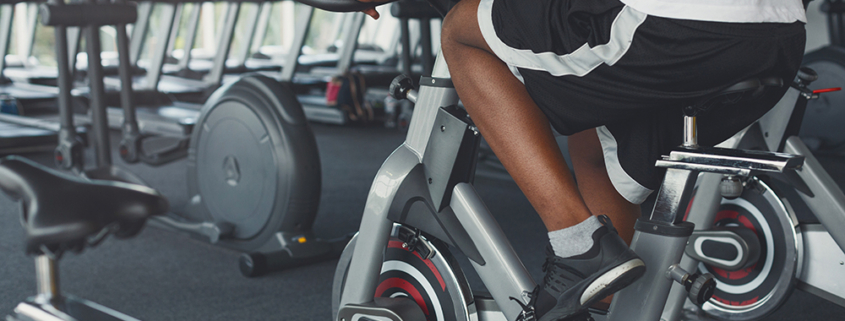 Young unrecognizable man on exercise bike in gym. Male legs in fitness club. Healthy lifestyle concept