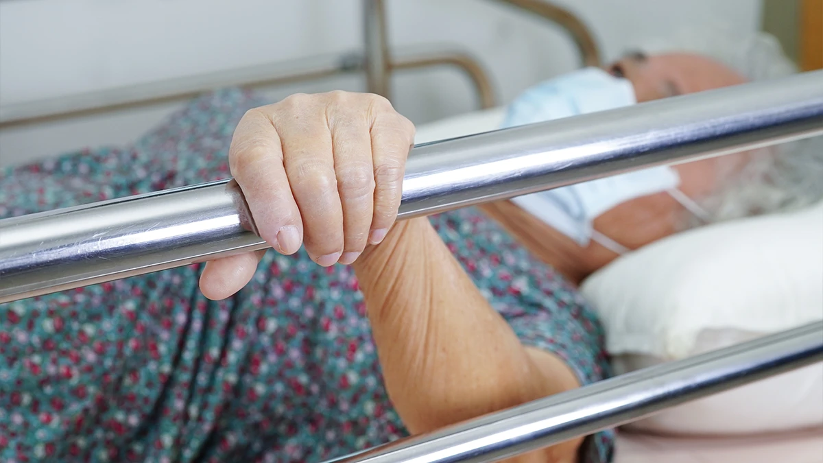 Injured elderly woman grabs the rail of her hospital bed while she waits for her family