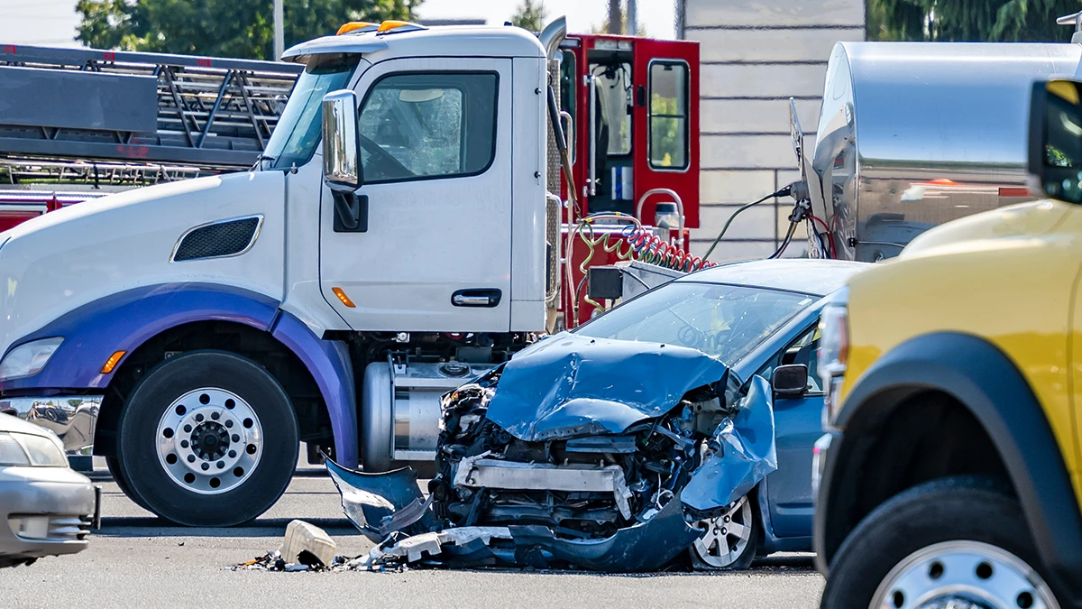 A collision between a semi and a blue car blocks a busy intersection.